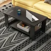 A dark gray coffee table with a laptop, a can, and a storage box on it, placed on a black and white patterned rug in front of a yellow sofa. Produktbild-Vorschau