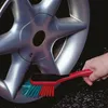 A hand is using a red and green brush to clean a silver car wheel. Produktbild-Vorschau