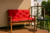 A red cushion on a wooden bench on a balcony with a small table and a mug. Produktbild-Vorschau