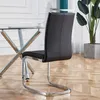 A black leather dining chair with a chrome frame is shown from the side, next to a glass-topped dining table with a chrome base. A large potted plant is visible in the background. Podgląd zdjęcia produktu