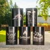 Five black metal barrels with decorative etchings are arranged in a staggered formation in an outdoor setting with greenery and gravel. Produktbild-Vorschau