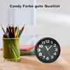 A black analog alarm clock sits on a wooden desk next to a cup of colored pencils and some books. Produktbild-Vorschau
