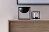 Two black decorative holders are placed on a wooden surface in front of a textured pink wall. Produktbild-Vorschau