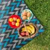 A picnic setup on the grass with a blanket, fruits, and bread. Náhľad obrázku produktu