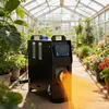 A black diesel heater is placed in a greenhouse surrounded by plants and flowers, with warm air being emitted from the front. Voir les images du produit
