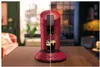 A split image shows a red coffee machine on a wooden table. The left side features the coffee machine with a cup of coffee and a blurred background of a living room. The right side shows the coffee machine in a darker, interior setting. Produktbild-Vorschau