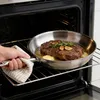 A hand holding a frying pan with a steak cooking inside an oven. Náhled obrázku produktu