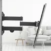 A black TV wall mount is attached to a concrete wall, extending outwards with its arms. A flat-screen TV is attached to the end of the mount, angled slightly. In the background, a living room setting with a sofa and coffee tables is visible. Voir les images du produit
