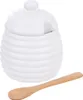 A white ceramic honey pot with a lid and a wooden spoon. Náhled obrázku produktu