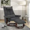 A dark gray recliner chair with a matching ottoman is placed in a living room setting, next to a floor lamp and a small side table. Produktbild-Vorschau