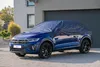 A blue car covered with a dark blue car cover is parked on a paved driveway in front of a modern house with a garage door. Anteprima dell’immagine prodotto