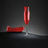 A red Bamix immersion blender and its stand are displayed on a dark, reflective surface against a gradient gray background. Podgląd zdjęcia produktu