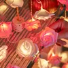 A hand is holding a string of rose-shaped LED lights, with other lights visible in the background. Produktbild-Vorschau