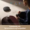 A woman is using a coffee grinder next to a robot vacuum cleaner and a smart speaker, with logos for voice assistants. Produktbild-Vorschau