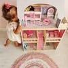 A young child is playing with a large wooden dollhouse. Voir les images du produit