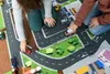 Children playing with toy cars on a play mat depicting a town. Produktbild-Vorschau