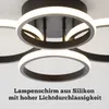 Close-up of a modern black LED ceiling lamp with multiple rings, illuminated with white light. Text overlay describes the lampshade material and light transmission. Náhľad obrázku produktu