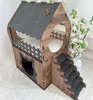 A wooden cat house with stairs and a paw print decoration, placed on a white fluffy surface with white flowers in the background. Voir les images du produit