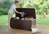 A woman is putting gardening tools into a storage box in a backyard. Podgląd zdjęcia produktu