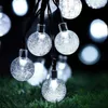 A string of solar-powered globe lights with a textured, bubble-like interior, resting on green grass at night. Produktbild-Vorschau