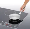A hand holding an induction hob adapter plate over an induction hob. Anteprima dell’immagine prodotto