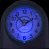 A close-up of a blue-lit analog alarm clock. Produktbild-Vorschau
