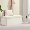 A cream-colored storage ottoman with a pillow on top, placed in a room with a wall and a doorway. Produktbild-Vorschau