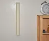 A beige cat scratching post is mounted vertically on a white wall next to a wooden shelf with a clock and small figurines. Produktbild-Vorschau