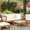 A patio lounge set with white cushions and a wooden coffee table is set up on a brick patio, surrounded by lush greenery and a wooden fence. Anteprima dell’immagine prodotto