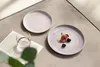 Two plates with fruit and a glass of water on a textured surface. Produktbild-Vorschau