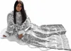 A woman is sitting on a fluffy white rug, wearing a grey blanket with sleeves that has a snowflake and reindeer pattern. Produktbild-Vorschau