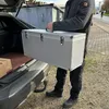 A person is loading a large silver case into the back of a car. Produktbild-Vorschau