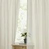 A close-up view of a beige linen curtain partially drawn, revealing a window with greenery outside and a small potted plant on a wooden table. Produktbild-Vorschau