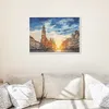 A framed painting of a European city square at sunset is displayed on a wall above a sofa. Podgląd zdjęcia produktu