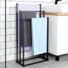 A black metal towel rack with three towels hanging on it, placed in a bathroom with white subway tiles and gray floor tiles. Náhľad obrázku produktu