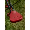 A close-up view of a red swing seat on a playground structure, with green grass in the background. Produktbild-Vorschau