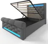 A grey upholstered bed frame with the mattress support lifted, revealing storage space underneath. Blue LED lights are integrated into the base and headboard. Produktbild-Vorschau