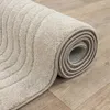 A rolled-up beige rug with a textured pattern is shown on a wooden floor. Produktbild-Vorschau
