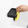 A hand is holding a yellow sponge, placing it into a black sink caddy that is attached to the edge of a white sink. Náhled obrázku produktu
