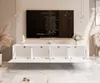 A modern living room with a white TV lowboard mounted on the wall, featuring open cabinets and a large television above it. Produktbild-Vorschau