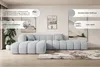 A light blue sectional sofa is shown in a modern living room setting with artwork on the walls and a rug on the floor. Produktbild-Vorschau