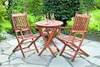 A wooden garden furniture set with two chairs and a table, set on a stone patio surrounded by greenery. Náhled obrázku produktu