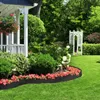 A garden scene with a porch, flower beds, and a white arbor. Produktbild-Vorschau