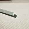 A close-up view of a green and white U-shaped profile strip, likely a protective edge or seal, resting on a textured light-colored surface. Voir les images du produit