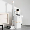 A white and orange cordless vacuum cleaner is standing in its charging station next to a white cabinet. The product is illuminated with soft light, creating a shadow on the wall behind it. Produktbild-Vorschau