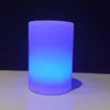 A cylindrical lamp emitting purple and blue light, placed on a white surface against a black background. Produktbild-Vorschau