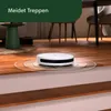 A white robot vacuum cleaner is shown on a wooden floor near the edge of a step, with a green overlay at the top of the image. Náhľad obrázku produktu