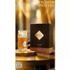 A perfume bottle and its box are displayed on a table with a blurred golden background. Podgląd zdjęcia produktu