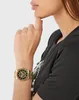A woman wearing a black t-shirt and a gold watch with colorful accents on her wrist. Anteprima dell’immagine prodotto