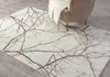 A rug with a branch pattern is placed in a living room setting next to a chair with a blanket. Náhled obrázku produktu